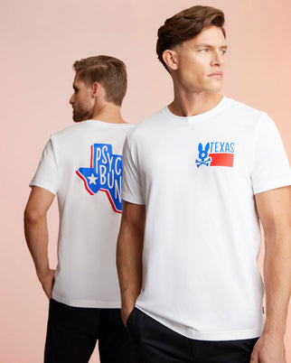 Two models wear matching white Psycho Bunny t-shirts made from Pima cotton jersey, with "Texas" in blue and red and a star logo on the front. The shirts also feature a Bunny logo graphic on the back. Both are standing against a light pink background.