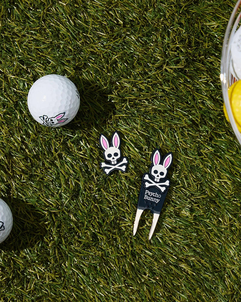 A green expanse features a golf ball adorned with a bunny skull logo, accompanied by two matching bunny skull ball markers and the DIVOT TOOL - B6A699C200, which is black and branded with 