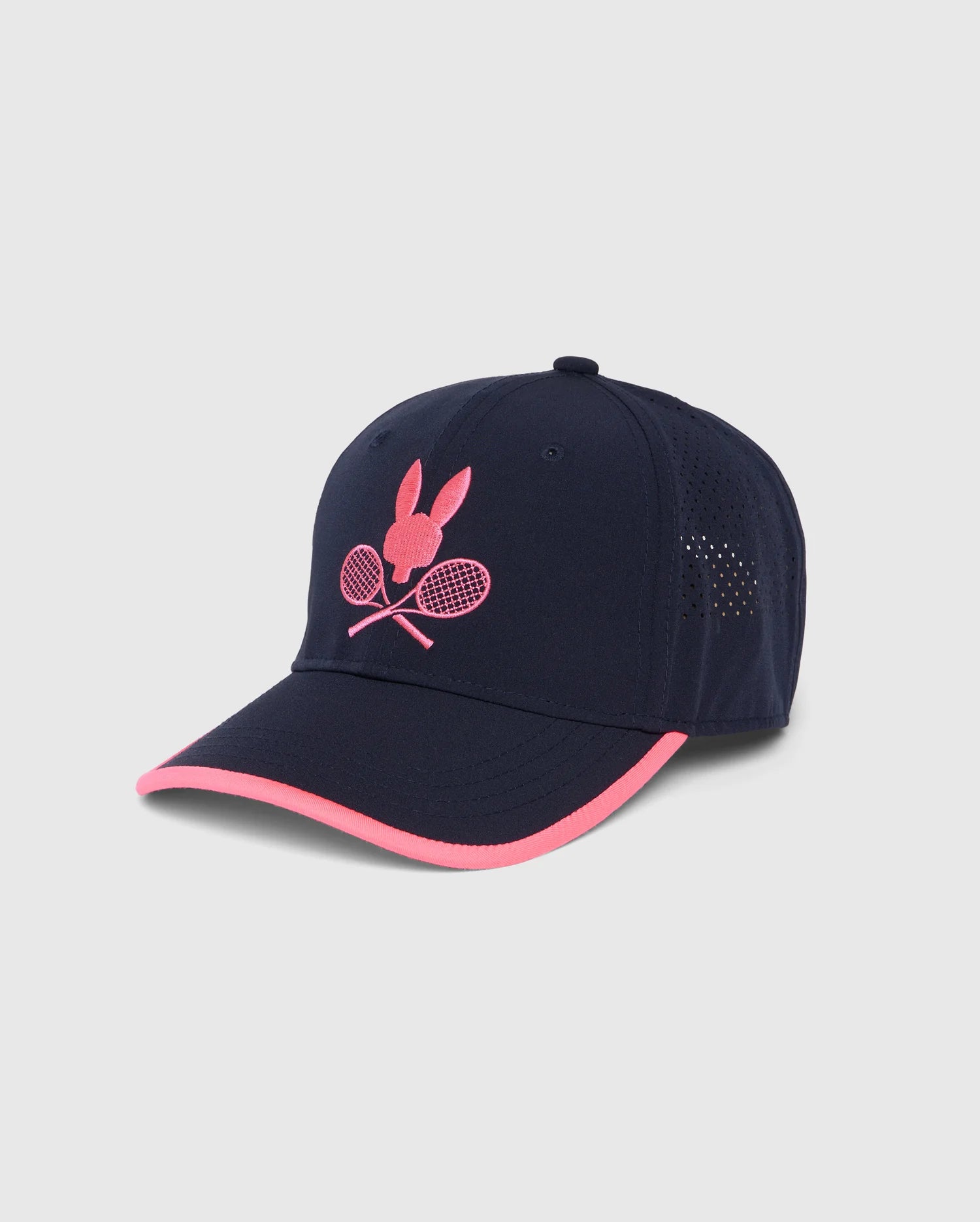 A navy blue baseball cap with pink accents, featuring a pink Bunny design logo on the front with crossed tennis rackets. The sides of the cap have small perforations for ventilation. The pink brim edge contrasts with the navy blue cap, perfect for fans of the National Bank Open in Montreal. This is the KIDS MONTREAL TOURNAMENT CAP - B0A703C200 by Psycho Bunny.