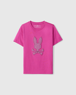 A bright pink short-sleeved T-shirt made from luxurious Peruvian Pima cotton, featuring an HD-silicone design of a bunny head with crossbones underneath in the center. The KIDS RIVIERA GRAPHIC TEE - B0U639C200 by Psycho Bunny is displayed on a plain white background.