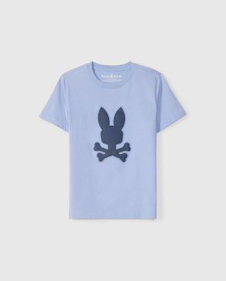 A light blue short-sleeve graphic tee crafted from luxurious Peruvian Pima cotton, featuring a dark blue graphic on the front of a rabbit head with crossed bones beneath it, resembling a playful skull and crossbones design. The label inside the collar reads "Psycho Bunny." This is the KIDS RIVIERA GRAPHIC TEE - B0U639C200 by Psycho Bunny.