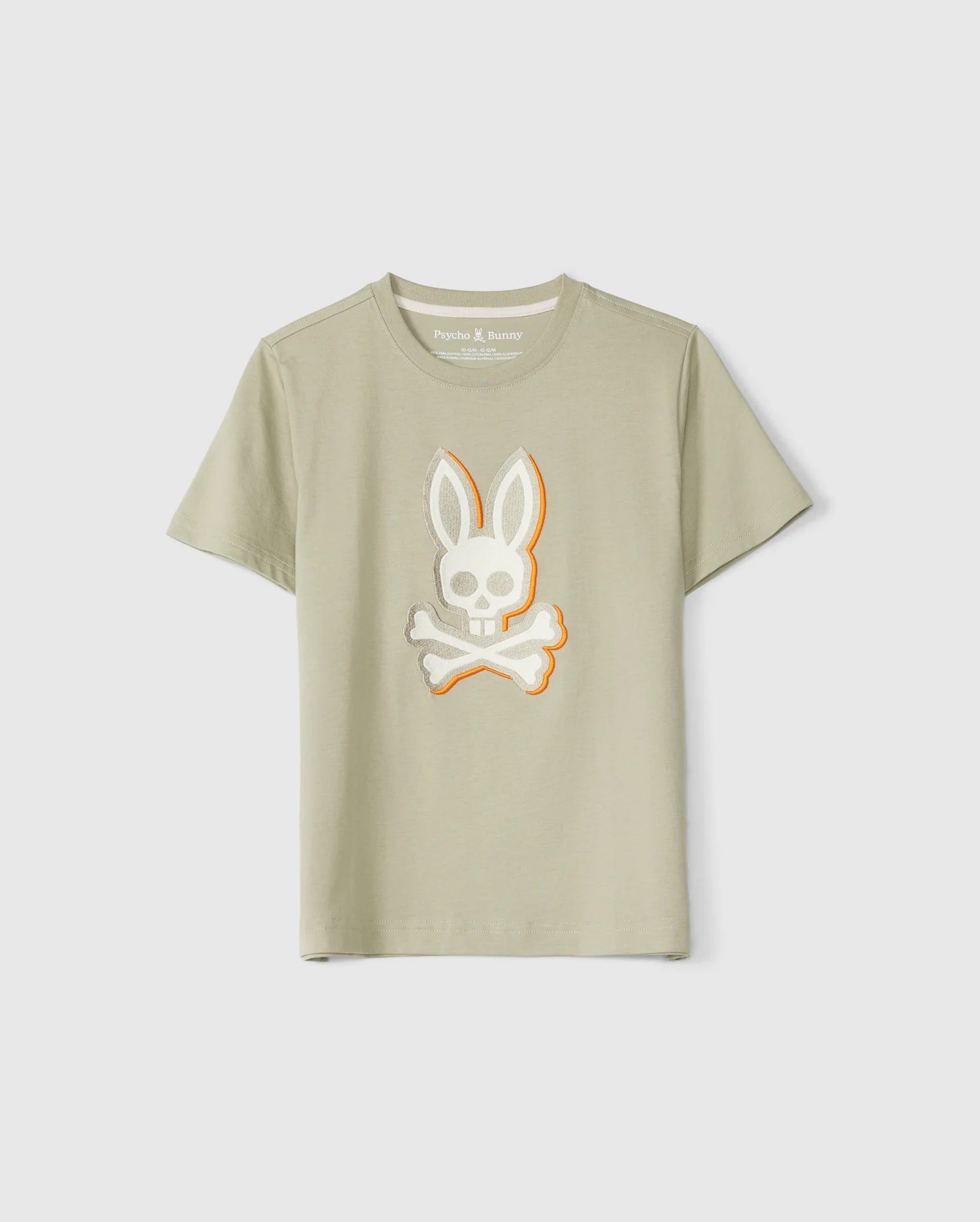 A light khaki Pima cotton tee with short sleeves, featuring a graphic of a bunny skull and crossbones in white and orange on the front. The shirt has a crew neckline and an embroidered logo, displayed against a plain, light grey background. Product: KIDS KAYDEN GRAPHIC TEE - B0U676C200 by Psycho Bunny.