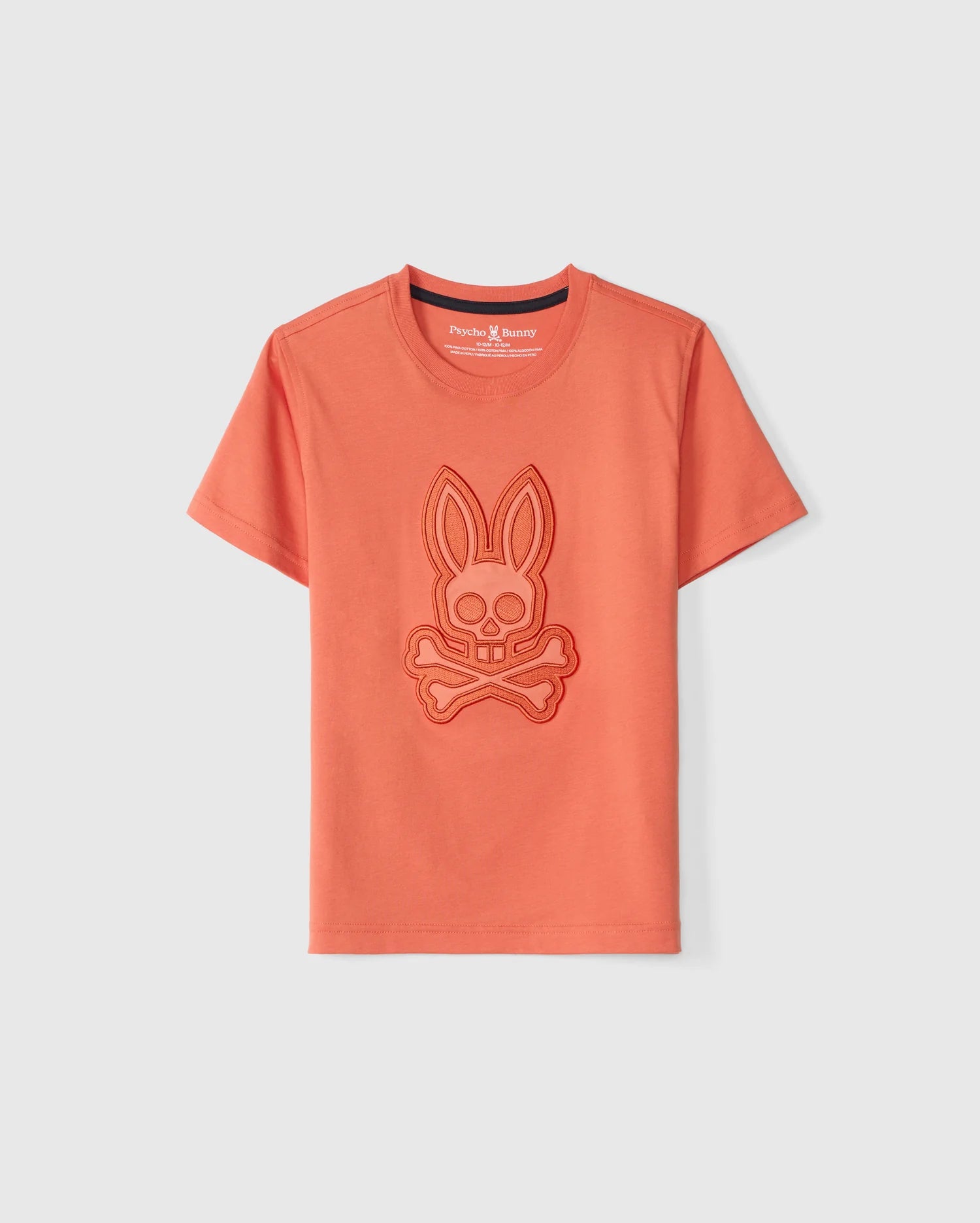 The KIDS MALTON GRAPHIC TEE - B0U795D200 from Psycho Bunny is an orange, Peruvian-crafted short-sleeve t-shirt featuring an embossed graphic of a bunny head with crossbones underneath on the front. The neckline has a contrasting dark trim on the inside, and the brand name 