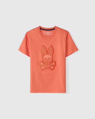 The KIDS MALTON GRAPHIC TEE - B0U795D200 from Psycho Bunny is an orange, Peruvian-crafted short-sleeve t-shirt featuring an embossed graphic of a bunny head with crossbones underneath on the front. The neckline has a contrasting dark trim on the inside, and the brand name "Psycho Bunny" is visible at the back of the neckline.