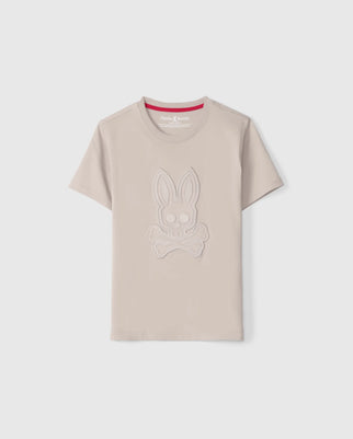 The KIDS MALTON GRAPHIC TEE - B0U795D200 by Psycho Bunny is a light beige short-sleeve T-shirt featuring a striking raised design of a bunny skull and crossbones on the front. Crafted meticulously from Peruvian Pima cotton, this tee has a crew neck collar with subtle red lining on the inside. The backdrop of the graphic is plain white.