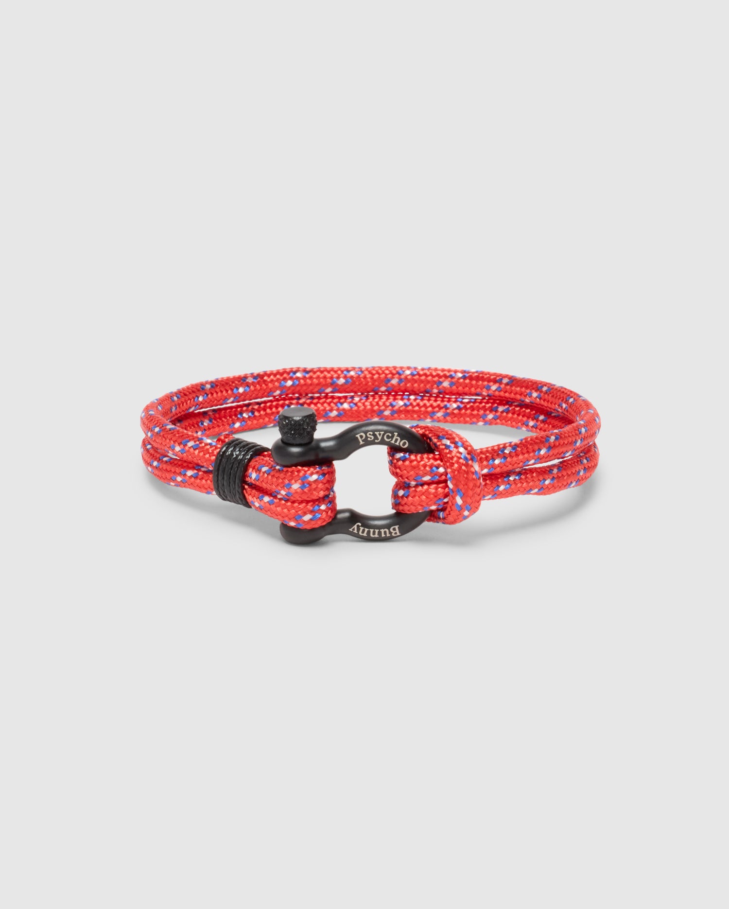 The Men's Rope Bracelet - B6A368E200 from Psycho Bunny is a stylish red and blue braided nylon cord accessory featuring a black zinc alloy clasp engraved with 