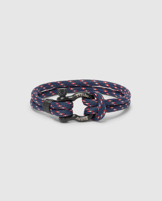 The Psycho Bunny MEN'S ROPE BRACELET - B6A368E200 is a stylish navy blue braided accessory with red and white speckles, featuring a modern lightweight design and an engraved metal clasp.