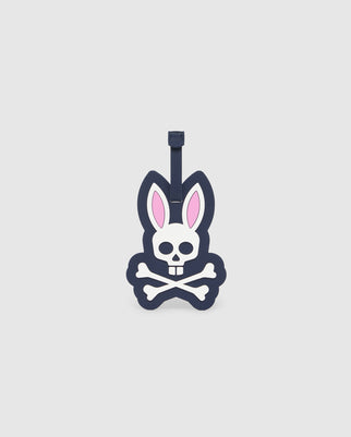 Introducing the MENS LUGGAGE TAG - B6A387B200 by Psycho Bunny: a playful and durable silicone luggage tag that combines a rabbit and a skull. It features bunny ears with pink inner detailing and crossbones beneath the skull, all presented in a bold monochrome color scheme. This fun travel accessory includes a strap for easy attachment to your bags.