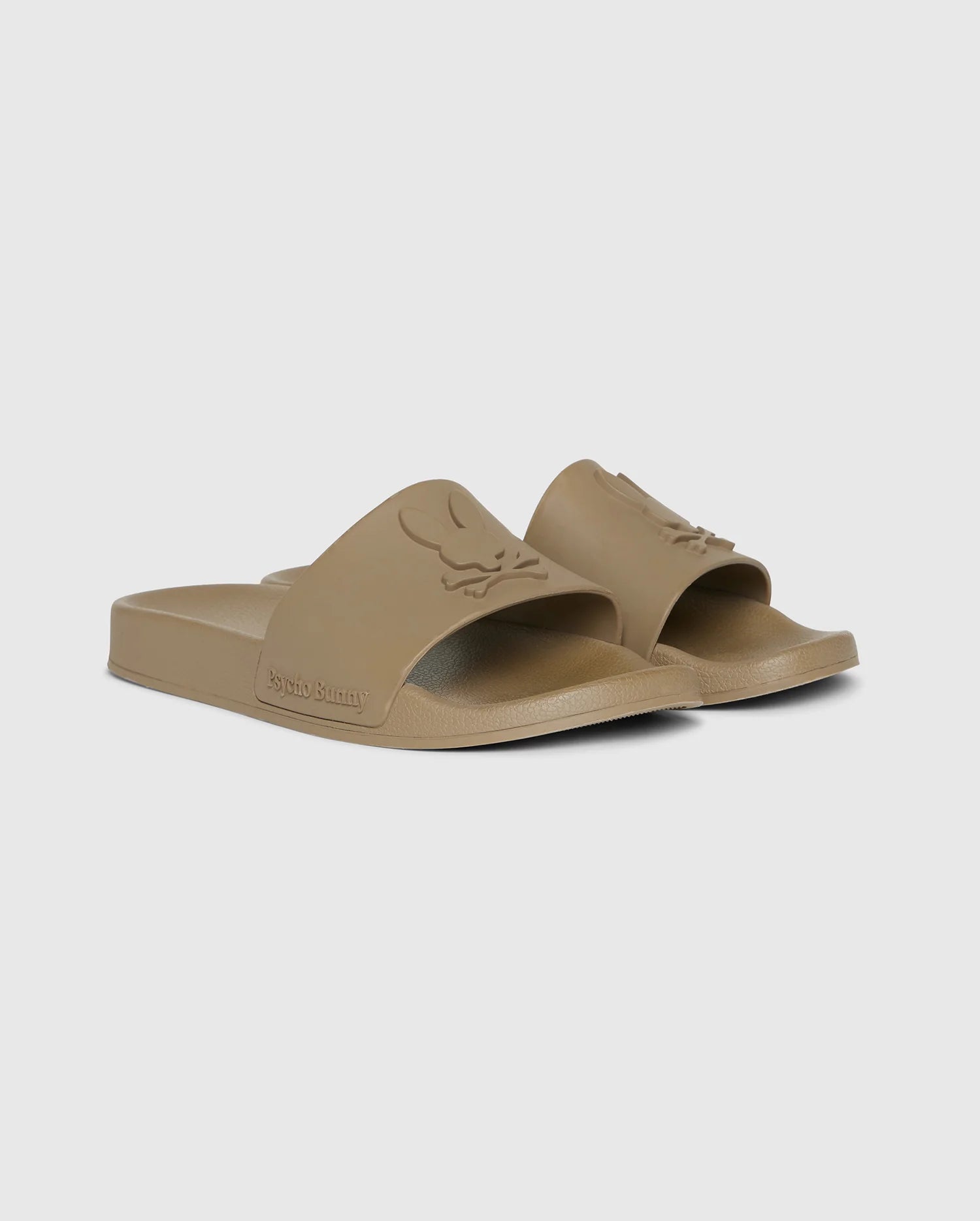 A pair of beige pool slides with an open-toe design and embossed logo on the strap. The molded footbed ensures comfort, while the slightly textured sole offers grip. The brand name 