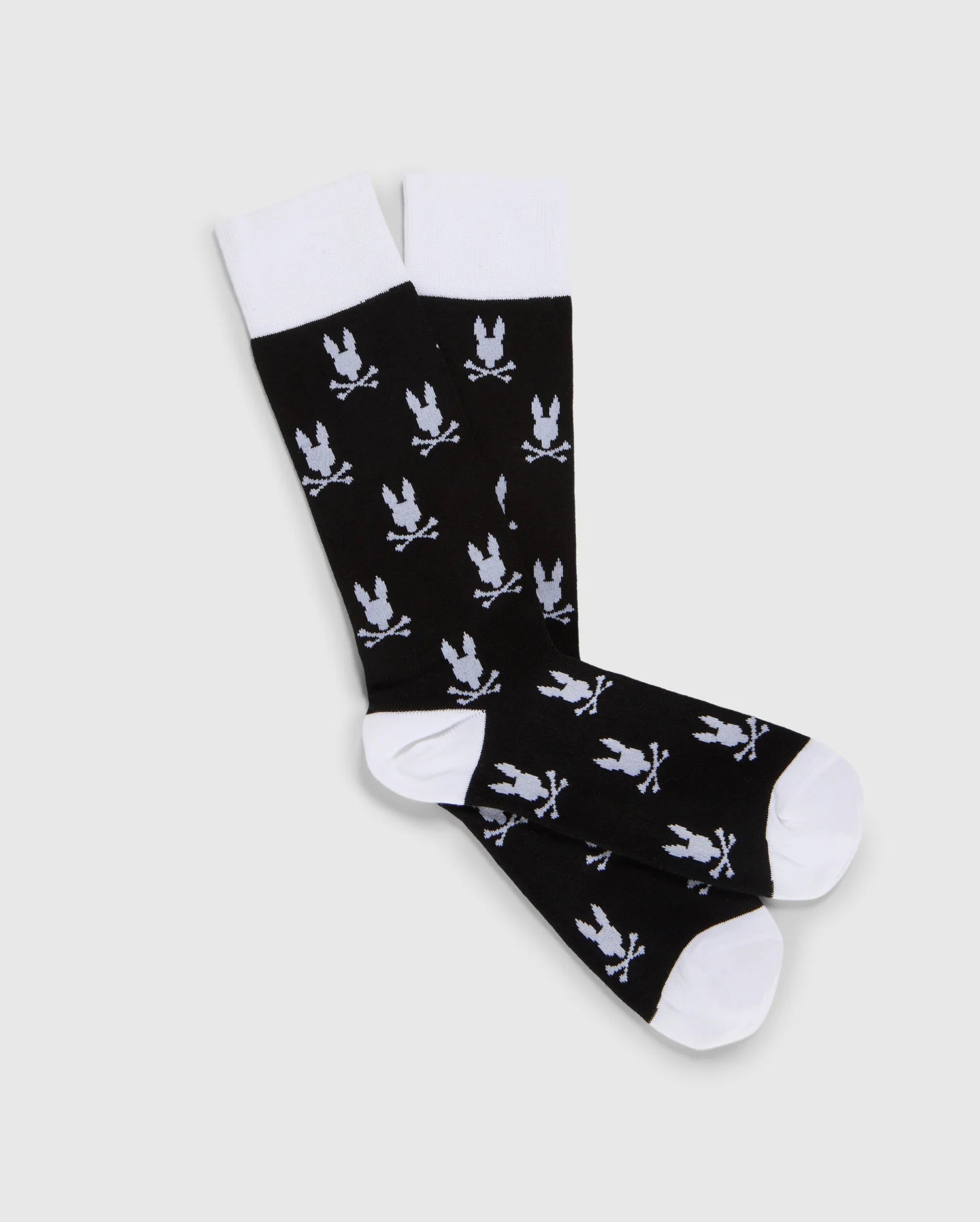 A pair of black dress socks with a jacquard-knit Bunny pattern and crossed swords, crafted from luxurious Peruvian Pima cotton. The toes, heels, and cuffs are white, contrasting with the black body. The MENS DRESS SOCK - B6F750B2SO by Psycho Bunny are laid flat on a plain light gray background.