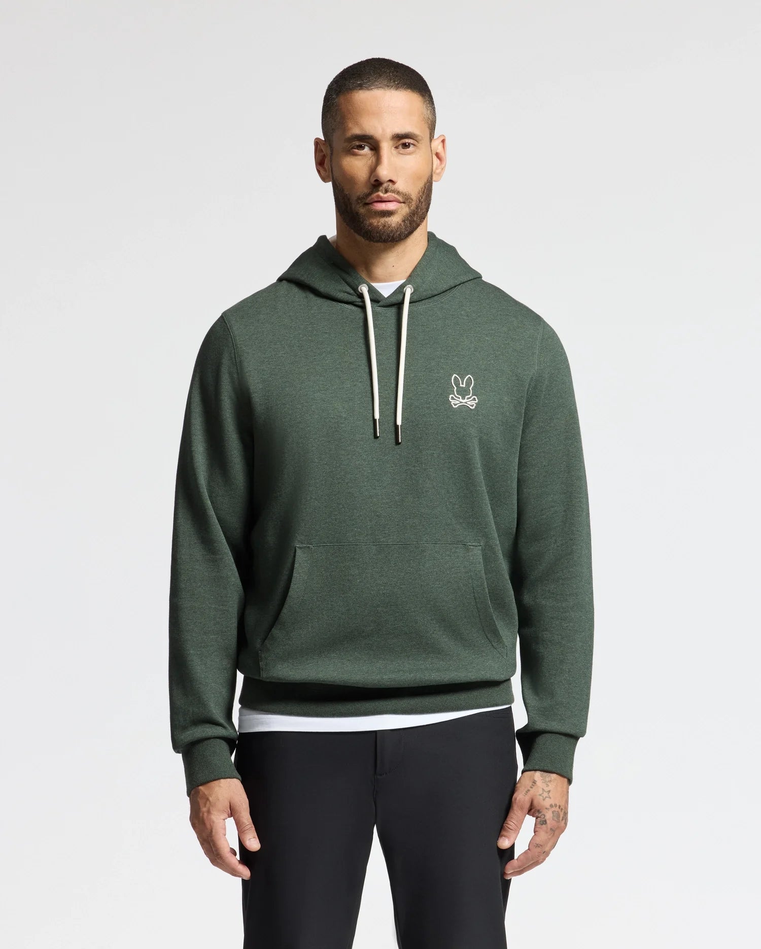 A man with short hair and a beard is wearing the stylish, lightweight Psycho Bunny MENS JAMES PREMIUM HOODIE - B6H789D200 in green. It features a white drawstring and a small embroidered logo on the chest. He stands against a plain white background, with his hands at his sides, paired with black pants.