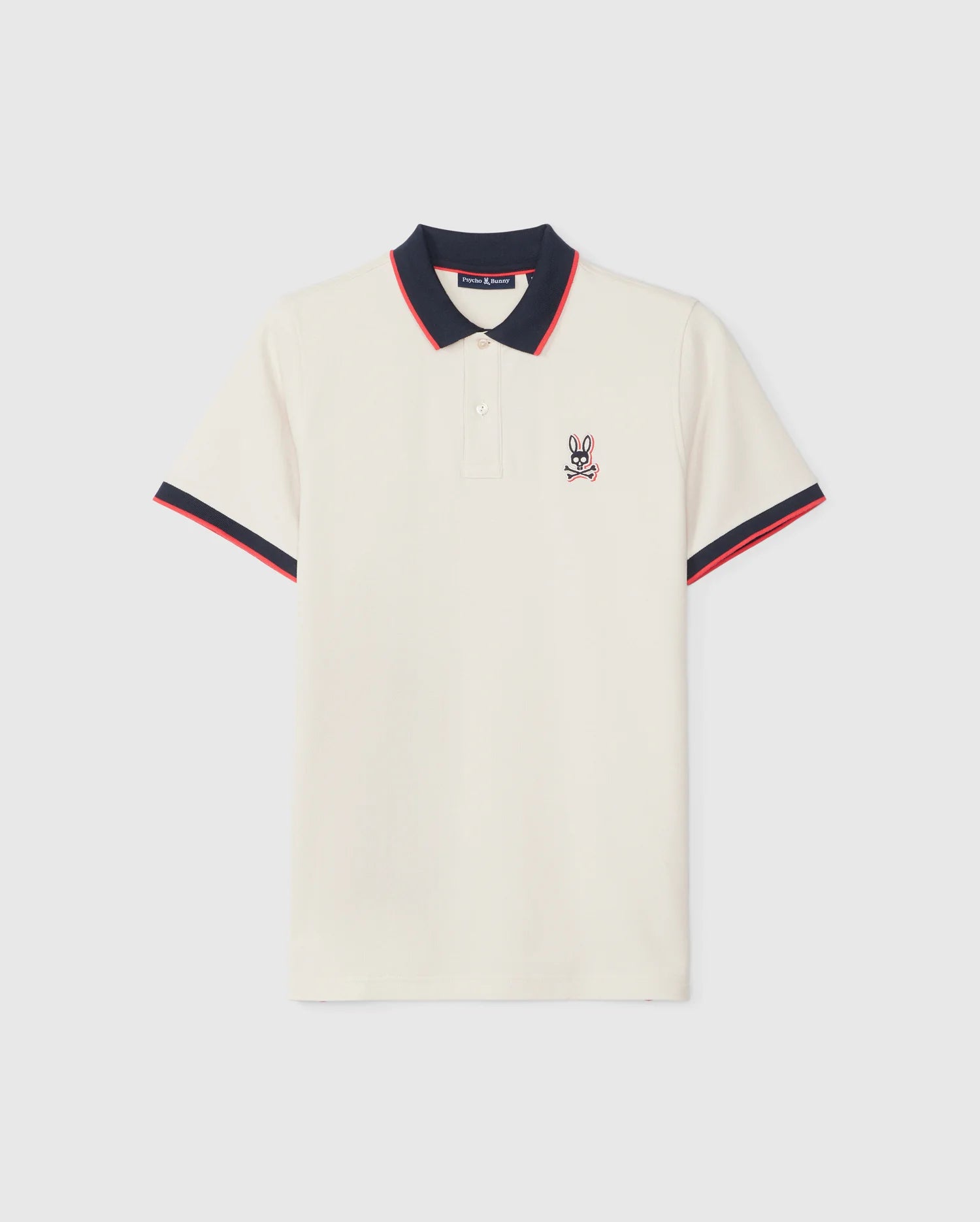 The Psycho Bunny Men's Kayden Pique Polo - B6K675C200 is crafted from diamond-knit Pima cotton piqué and features a white fabric with a navy blue collar and red trim. The sleeves mirror this trim, with the left chest boasting a small embroidered emblem of a bunny with crossed bones.