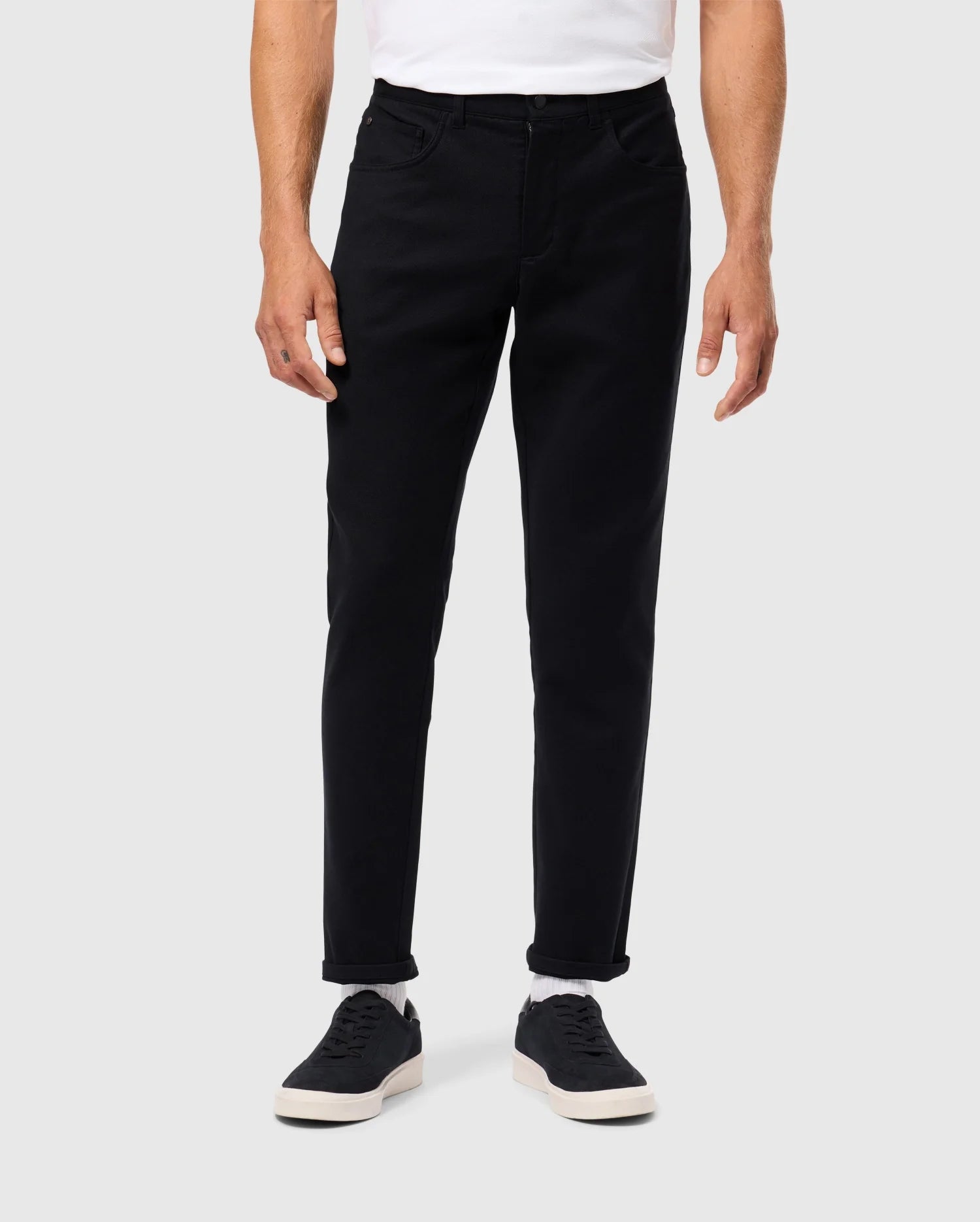 A person is wearing the Psycho Bunny MENS HAYS TWILL PANT in black (B6P894D200), crafted from a cotton-blend twill, along with a white shirt and black sneakers featuring white soles. The pants boast a straight fit and are slightly rolled up at the ankles for enhanced comfort, set against a plain, light-colored background.