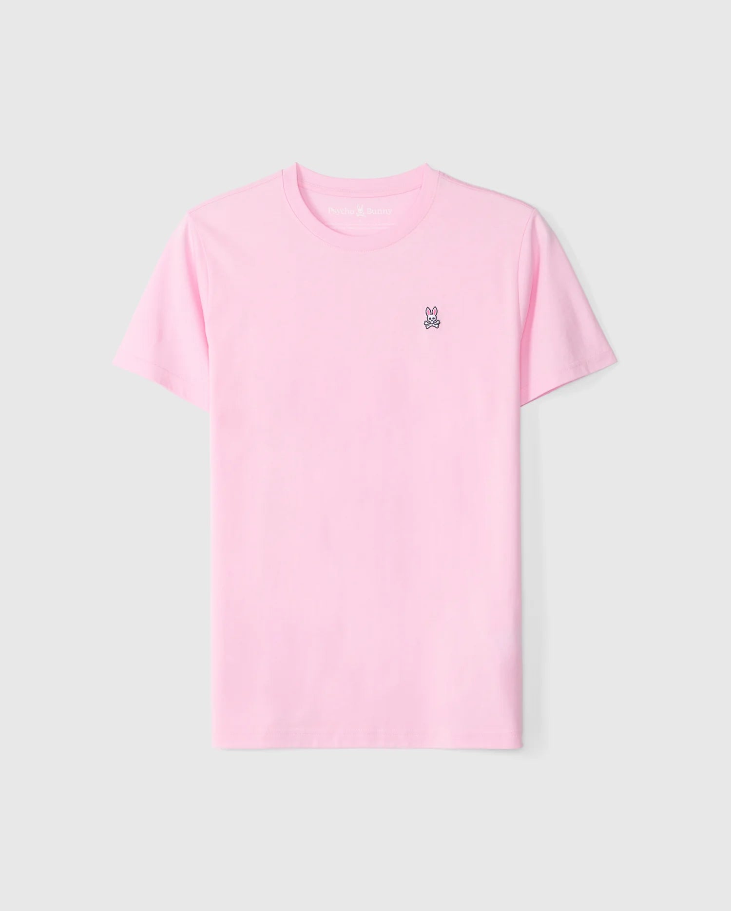 The Psycho Bunny Men's Classic Crew Neck Tee - B6U014CRPC, in a light pink color, is displayed against a plain white background. This soft and versatile pima cotton short-sleeve T-shirt features a small embroidered black outline of a bunny head on the left chest area.