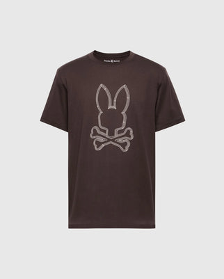 The Psycho Bunny Mens Monarc Front Bunny Graphic Tee (B6U211E200) showcases a stylized rabbit's head with ears above crossed bones in white on brown, crafted from 100% Pima cotton for unmatched softness and durability against a plain white background.