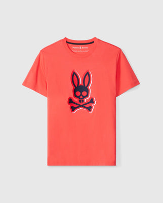 The MENS KAYDEN GRAPHIC TEE - B6U676C200 by Psycho Bunny is a vivid red short-sleeved graphic tee made from soft Pima cotton. It features a prominent black and red bunny head with crossbones graphic on the front and has a small neckline label that reads "Psycho Bunny." The T-shirt is showcased against a plain white background.