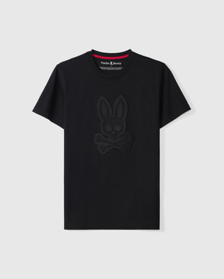 The MENS MALTON GRAPHIC TEE - B6U795D200 by Psycho Bunny features a black graphic design with a tonal bunny and crossbones at the center of the chest. Made from premium Pima cotton, it includes the "Psycho Bunny" label inside the neckline. The tee is set against a plain light gray background, highlighting its quality and style.