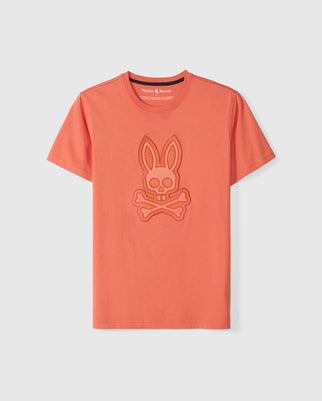 The Psycho Bunny MENS MALTON GRAPHIC TEE (B6U795D200) in coral orange features an embossed bunny skull and crossbones design on the chest. Made from luxurious Pima cotton, it offers short sleeves and a round neckline for comfort and style.