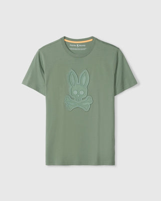 The Psycho Bunny MENS MALTON GRAPHIC TEE - B6U795D200 is a green short-sleeve graphic tee crafted from luxurious Pima cotton. It features an embroidered bunny skull and crossbones on the chest, along with a stylish orange accent on the inner neckline of the crew neck. Made in Peru, this tee offers exceptional quality and comfort.