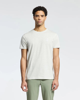 A person stands against a plain background, wearing a light gray MENS JAMES CREW NECK TEE from Psycho Bunny and olive green pants. They have short, curly hair and look directly at the camera with a neutral expression.