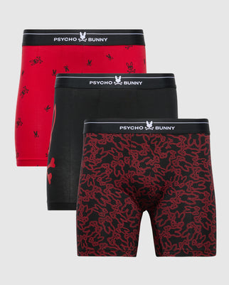 The MENS 3 PACK BOXER BRIEF - B6V198E200 from Psycho Bunny is a premium set featuring three briefs: one in solid red, another in solid black, and a third black with a red abstract design. Made from comfortable Pima cotton, each pair is adorned with the brand's logo on the waistband.