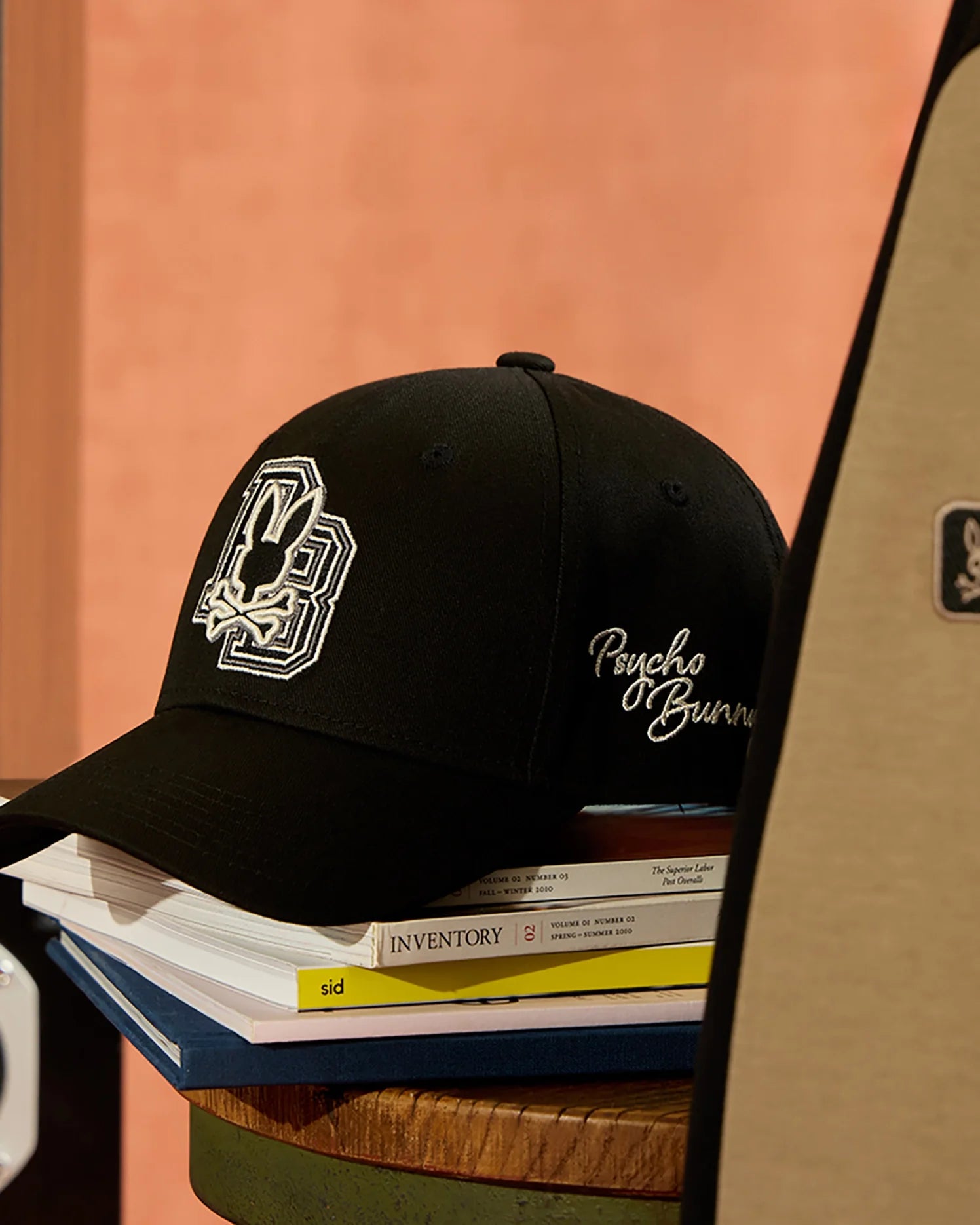 The MENS ZACK BASEBALL CAP - B6A886D200, a stylish black cap from Psycho Bunny made entirely of cotton and featuring an embroidered logo, is casually placed atop a stack of books, one of which is titled 